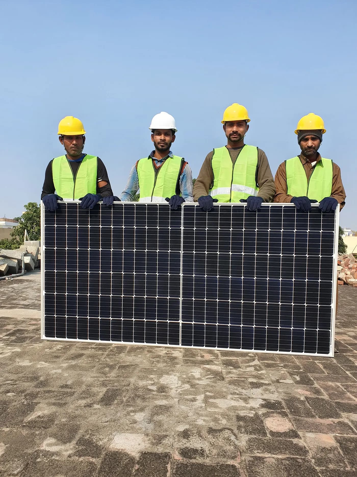 Four solar installers in hard hats holding a panel on a rooftop